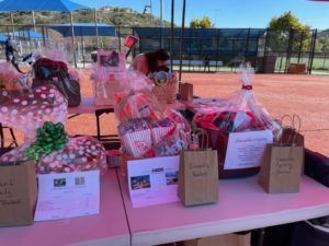 Gift baskets and brown paper bags displayed on a pink table at an outdoor event