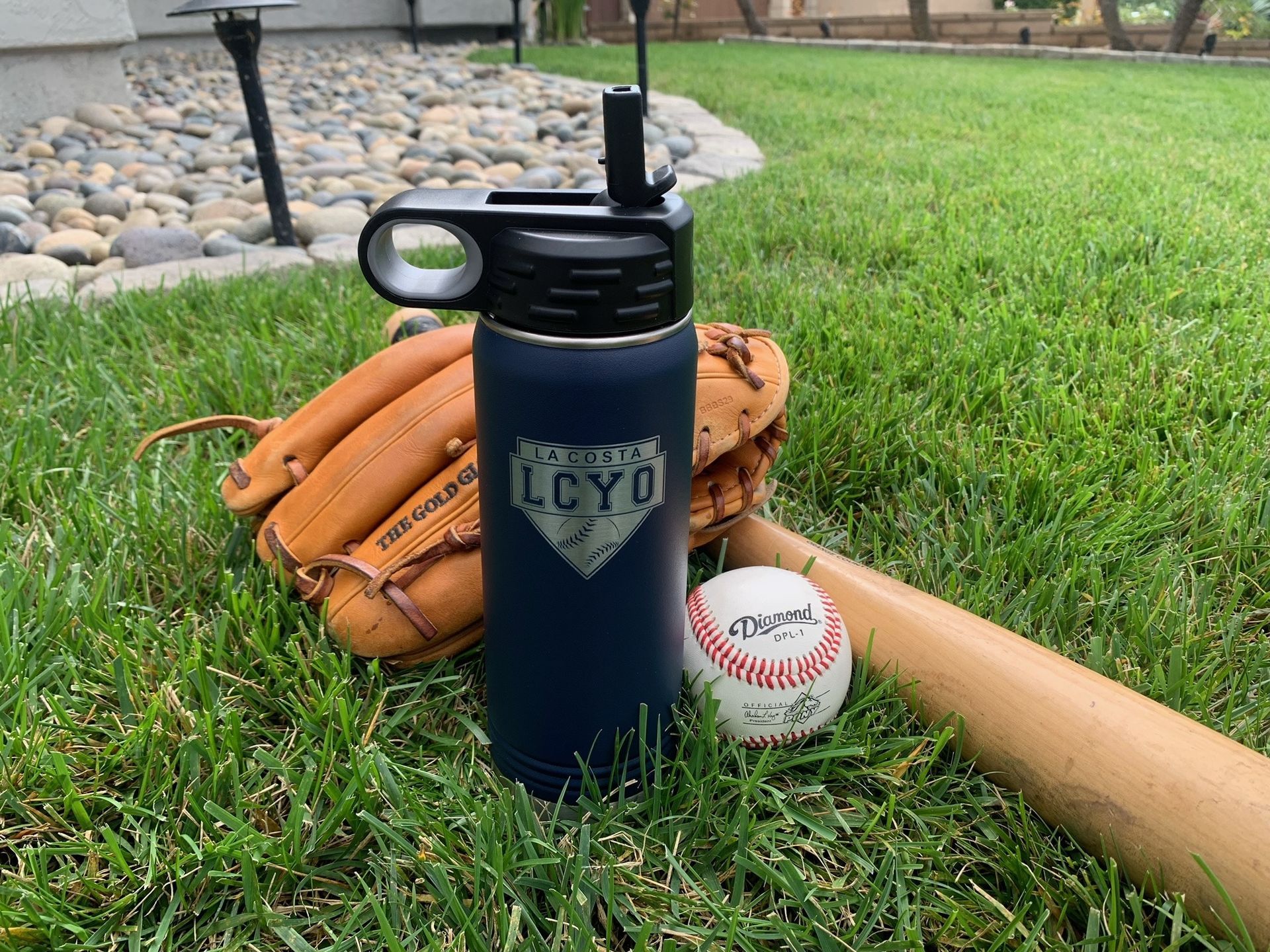 Baseball gear on grass: glove, bat, ball, and blue water bottle with straw.
