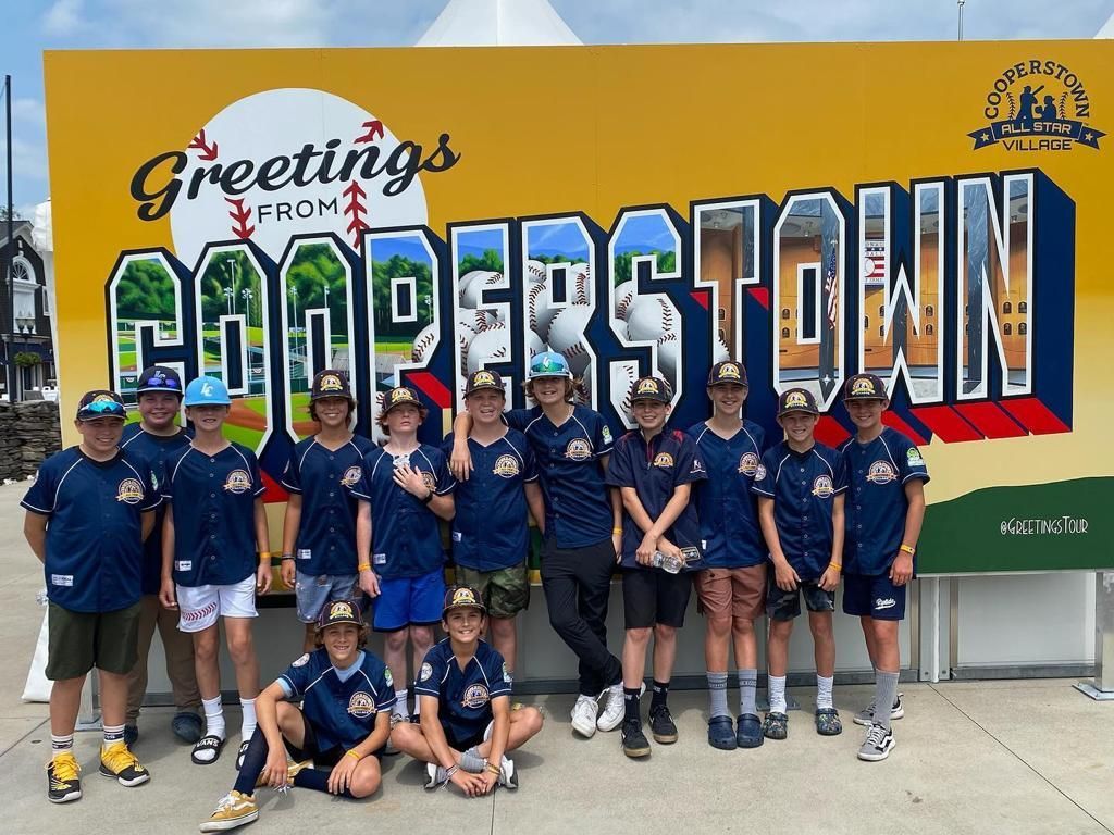 Youth group posing in front of the “Greetings from Cooperstown” sign on a sunny day