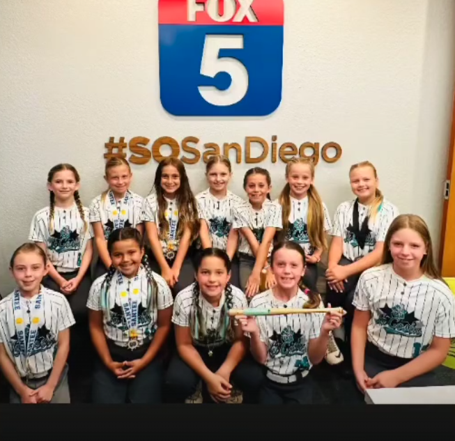 Children posing in matching shirts under a Fox 5 San Diego sign with #SOSanDiego backdrop