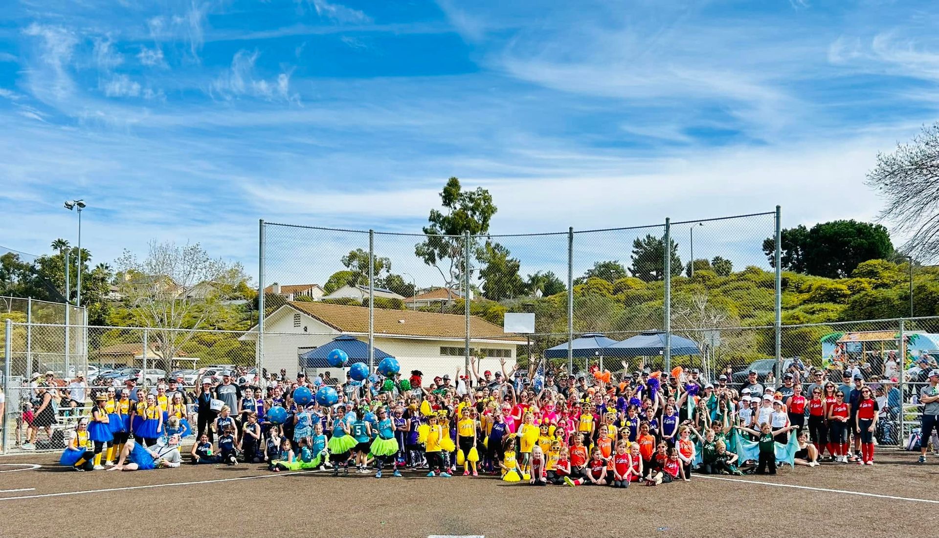 Large group posing on a soccer field, many wearing bright colored shirts and uniforms under a sunny sky