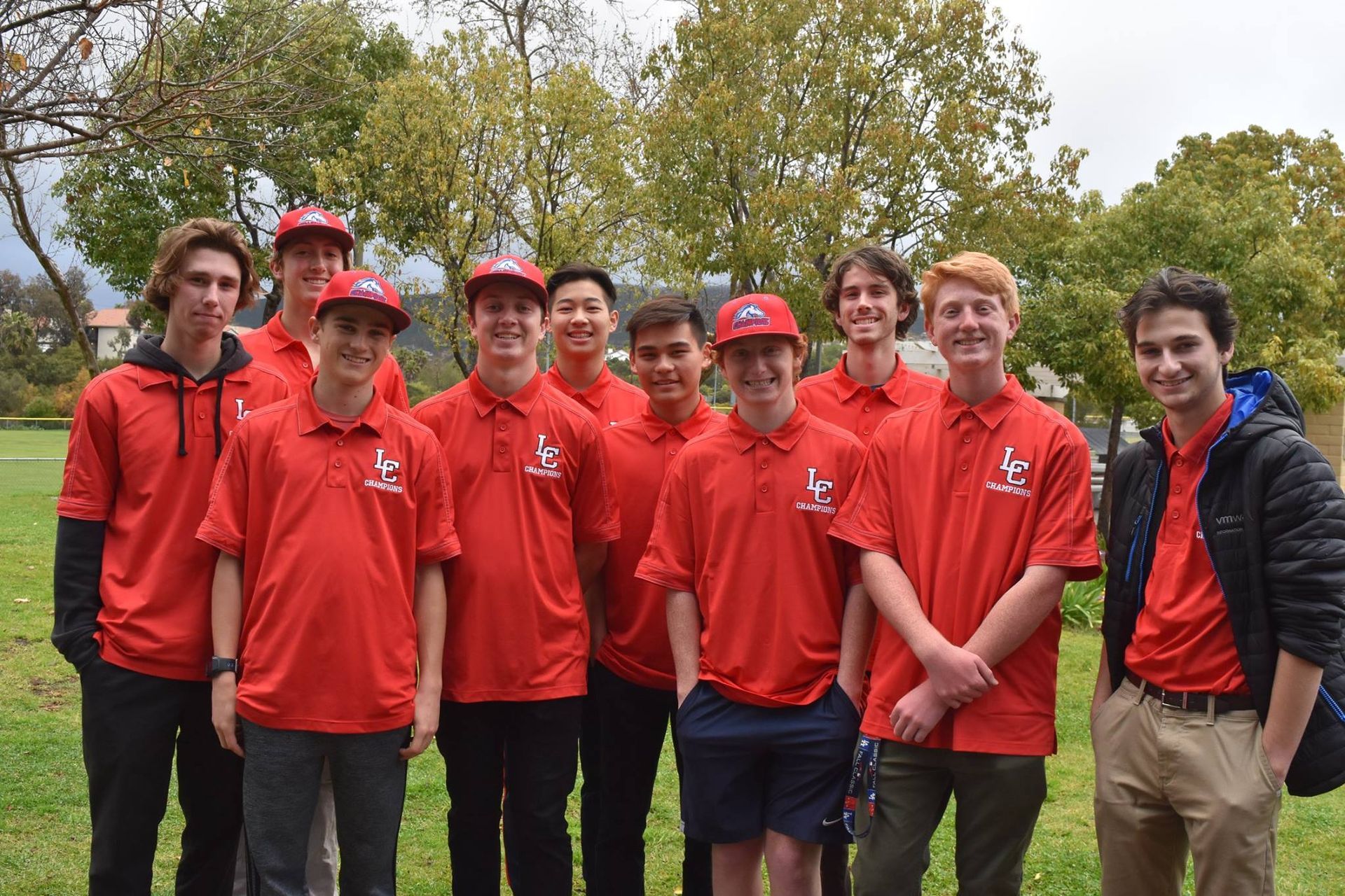 Group of people in red shirts and caps standing together outdoors in a park