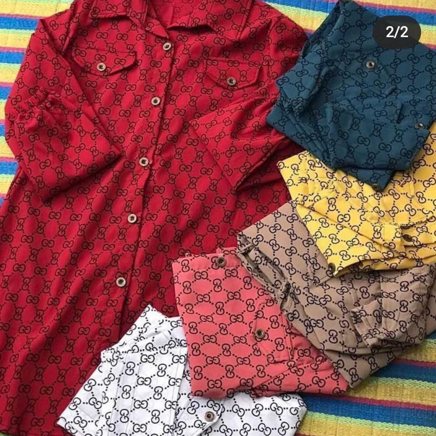 A red gucci shirt is sitting on top of a rainbow colored blanket.