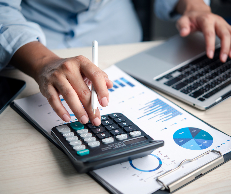 Person using a calculator, laptop, and reviewing financial documents with charts.