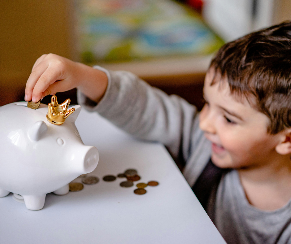 Young child putting coins into a white piggy bank, smiling.