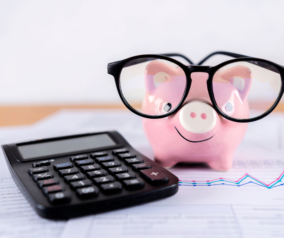 Pink piggy bank wearing glasses next to a calculator on a desk with financial papers.