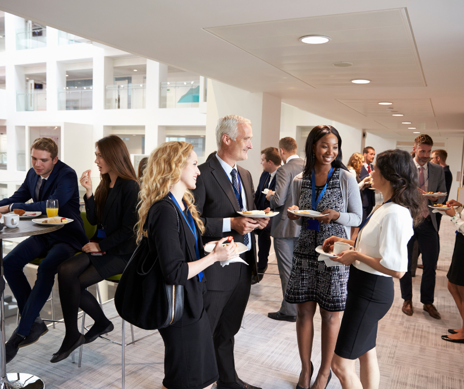 People at an event, socializing and eating food in a modern, open space.