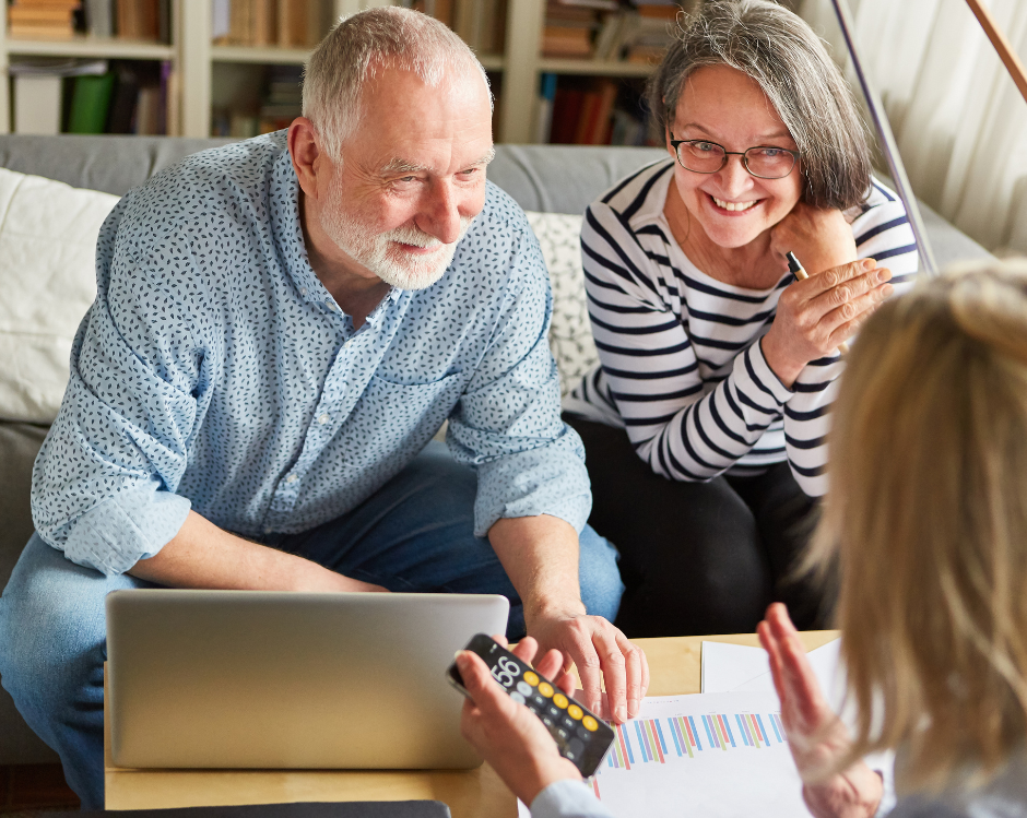 A couple consults with a financial advisor, looking at a laptop and holding a remote control.