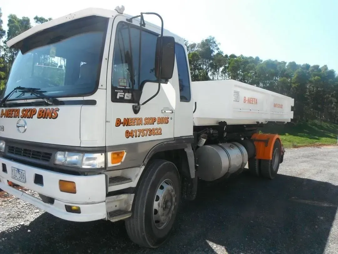 White dump truck parked on gravel road beside trees, with orange safety markings on the cab.