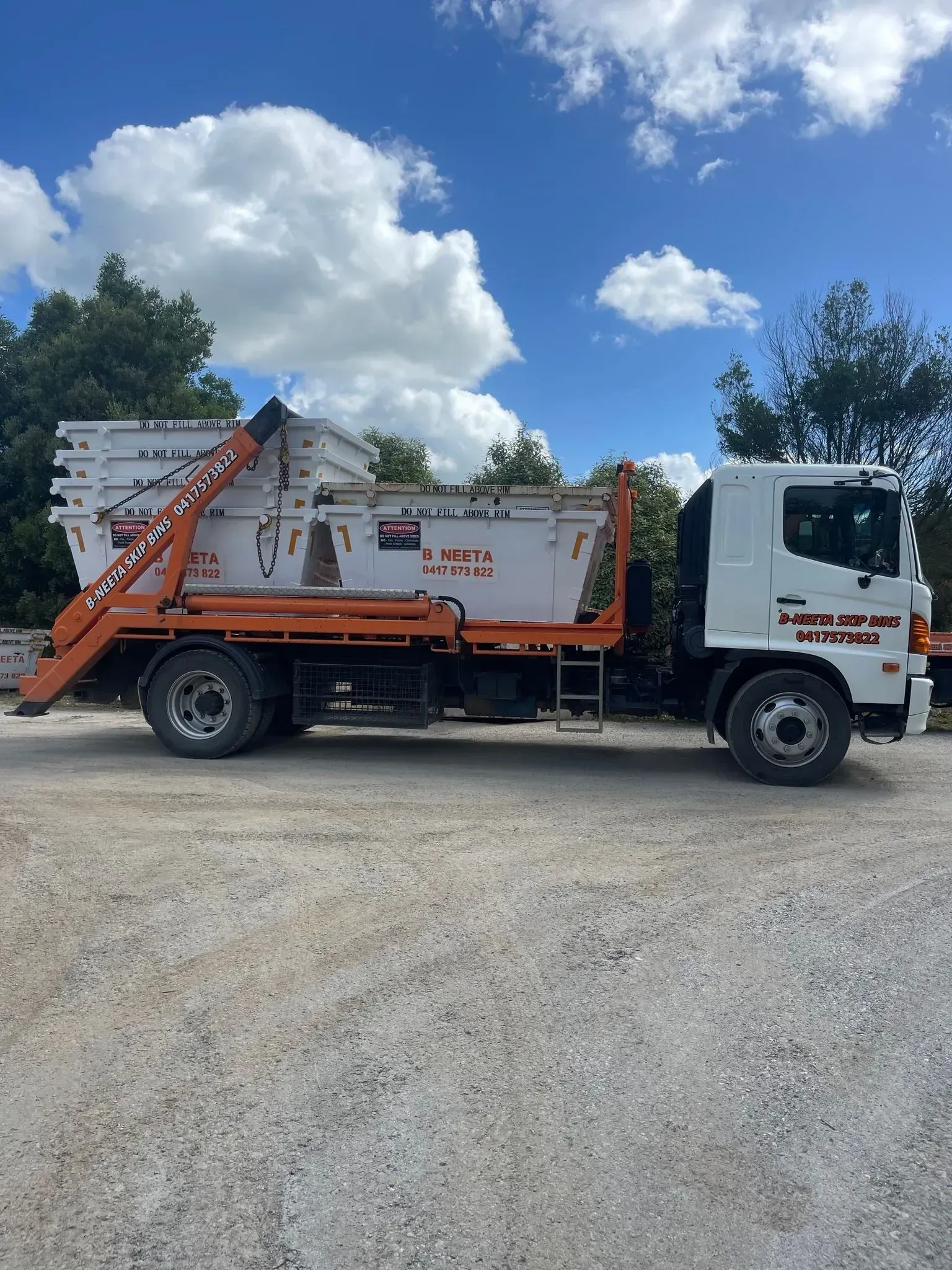 Orange utility truck with lift bed parked on gravel under a partly cloudy blue sky