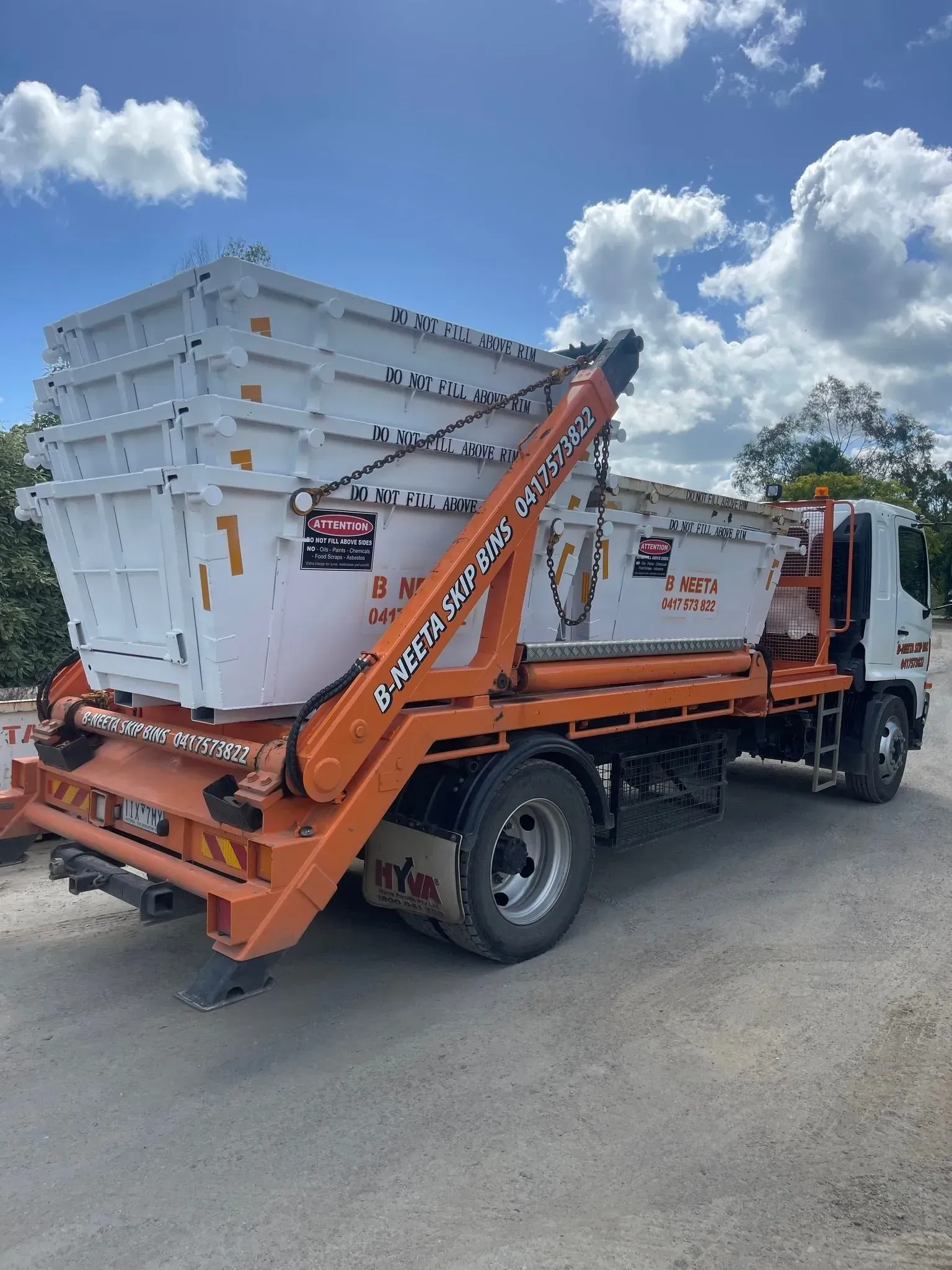 Orange dumpster truck carrying stacked white bins under a bright blue sky