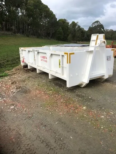 White industrial dumpster on a dirt road beside trees and grass