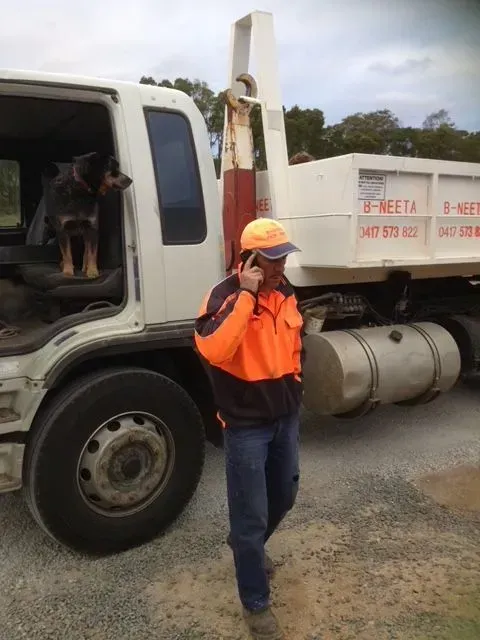 Worker in orange safety gear standing beside a white utility truck on a gravel roadside