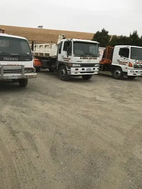 Three white Isuzu trucks parked on a gravel lot under an overcast sky.