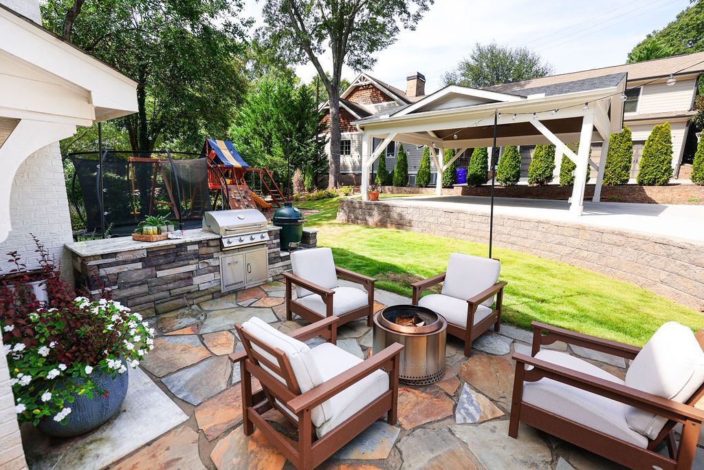 Patio seating area with cushioned chairs, fire pit, and stone walkway in a sunny backyard