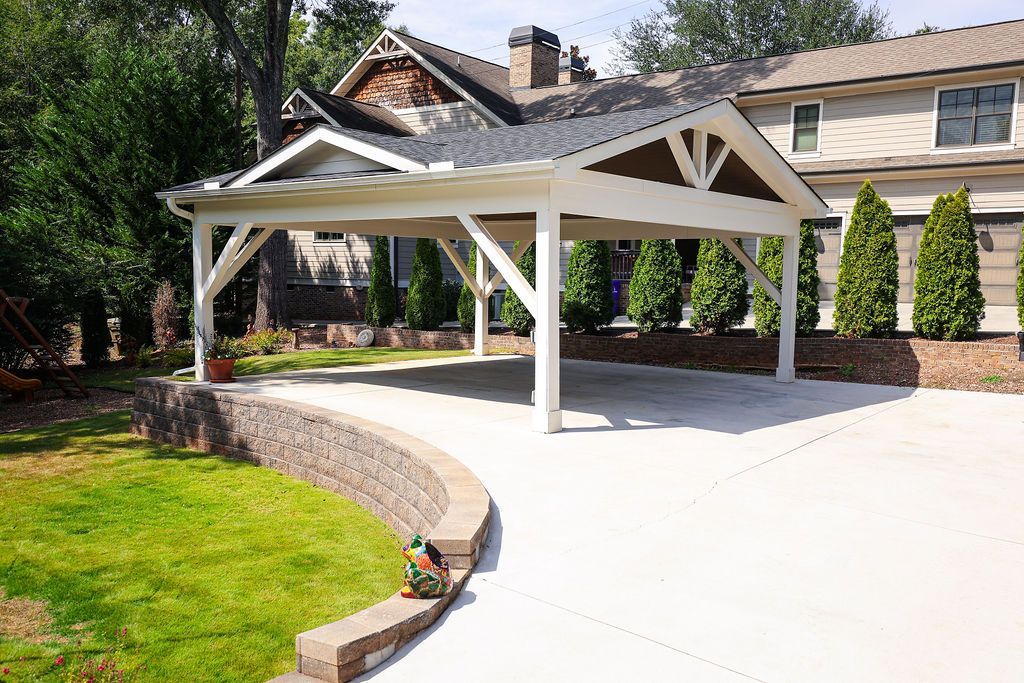 White outdoor pavilion on a curved concrete patio beside a green lawn and house