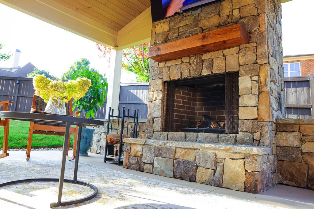 Covered stone patio with a brick fireplace, table, and outdoor seating area
