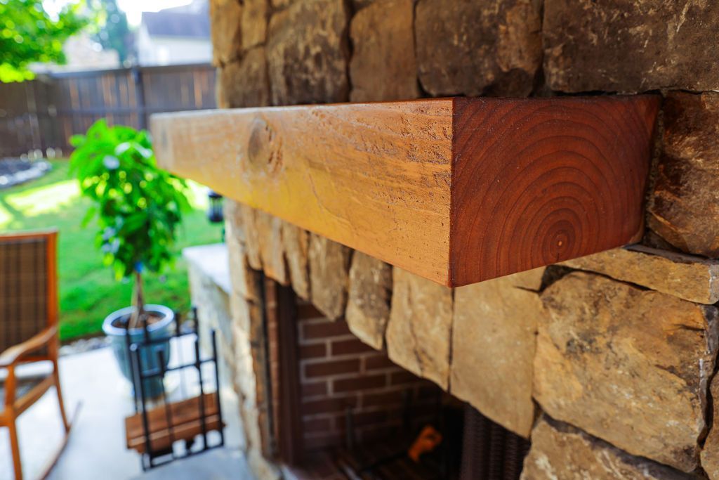 Stone fireplace mantel with a wooden shelf in a patio seating area