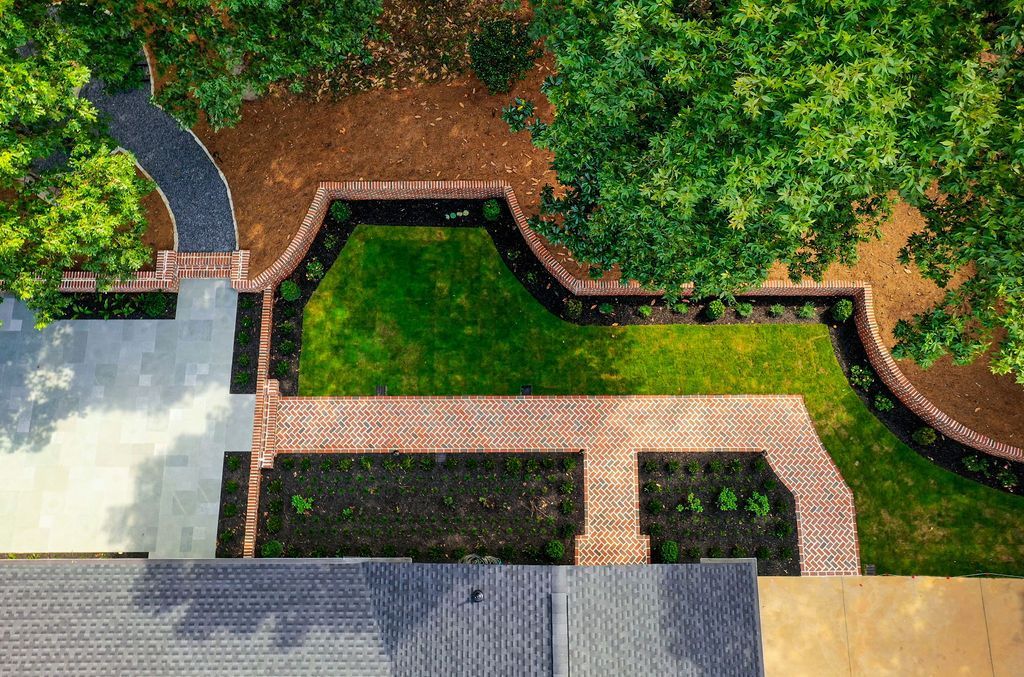 Aerial view of a landscaped garden with brick paths, green lawn, and surrounding trees.