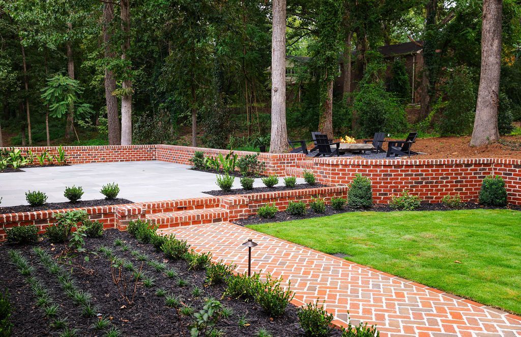 Landscaped garden with brick paths, red flower beds, green lawn, and tall trees