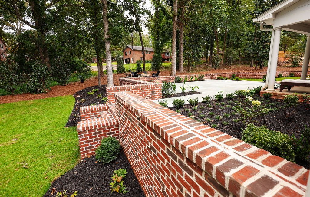 Brick garden wall bordering landscaped beds and a paved patio in a wooded yard