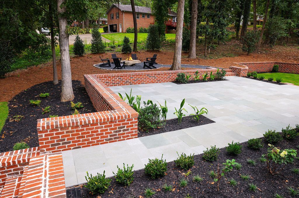 Brick-and-concrete courtyard with trees, raised flower beds, and mulch in a landscaped park area