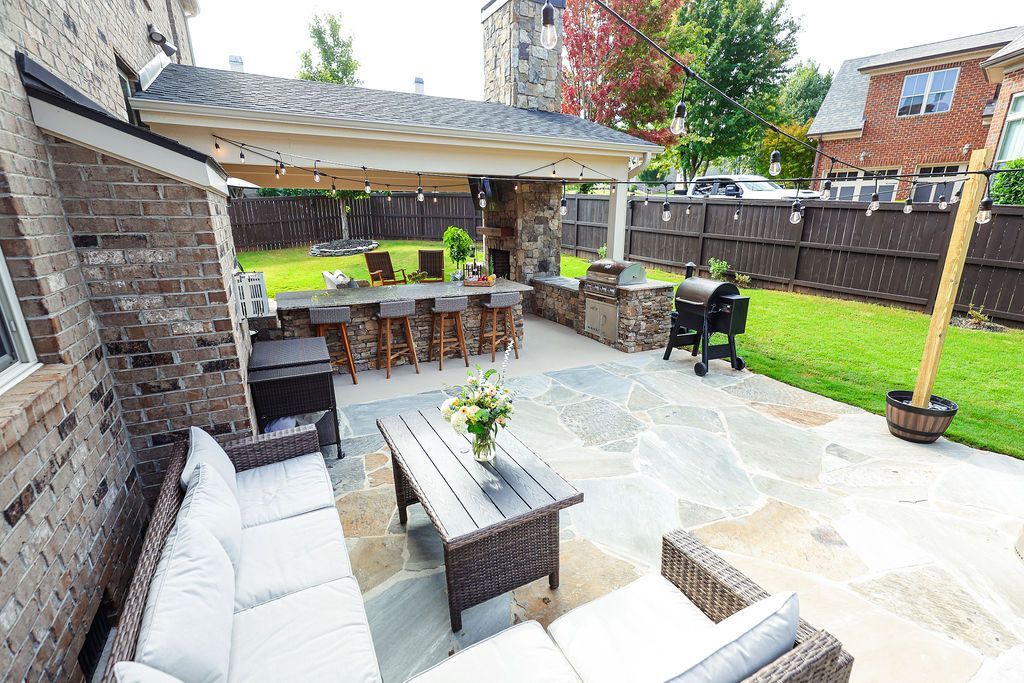 Patio with white sofa, woven chairs, dining table, pergola, and small lawn in a backyard