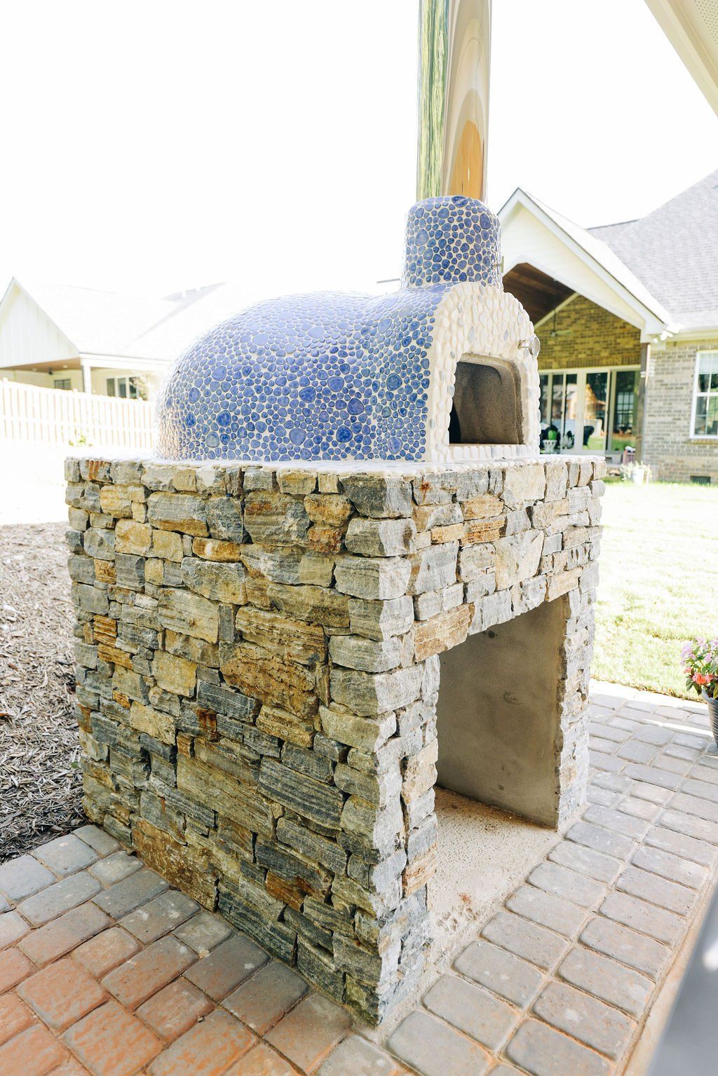 Stone outdoor pizza oven with a blue-tiled dome on a brick patio under a covered pavilion