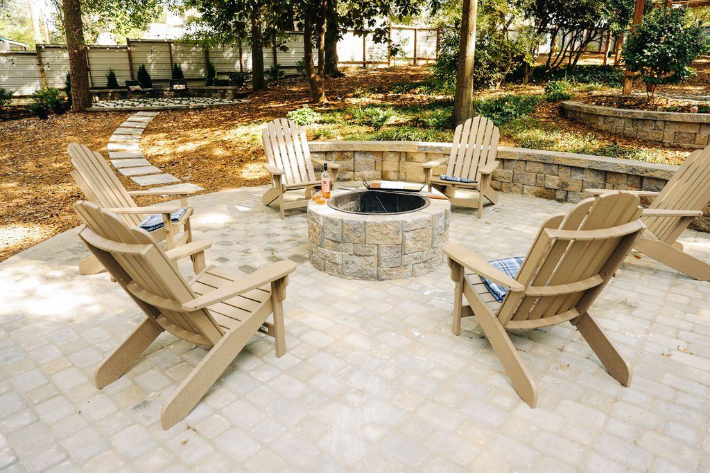Stone fire pit with four wooden chairs on a patio in a wooded backyard