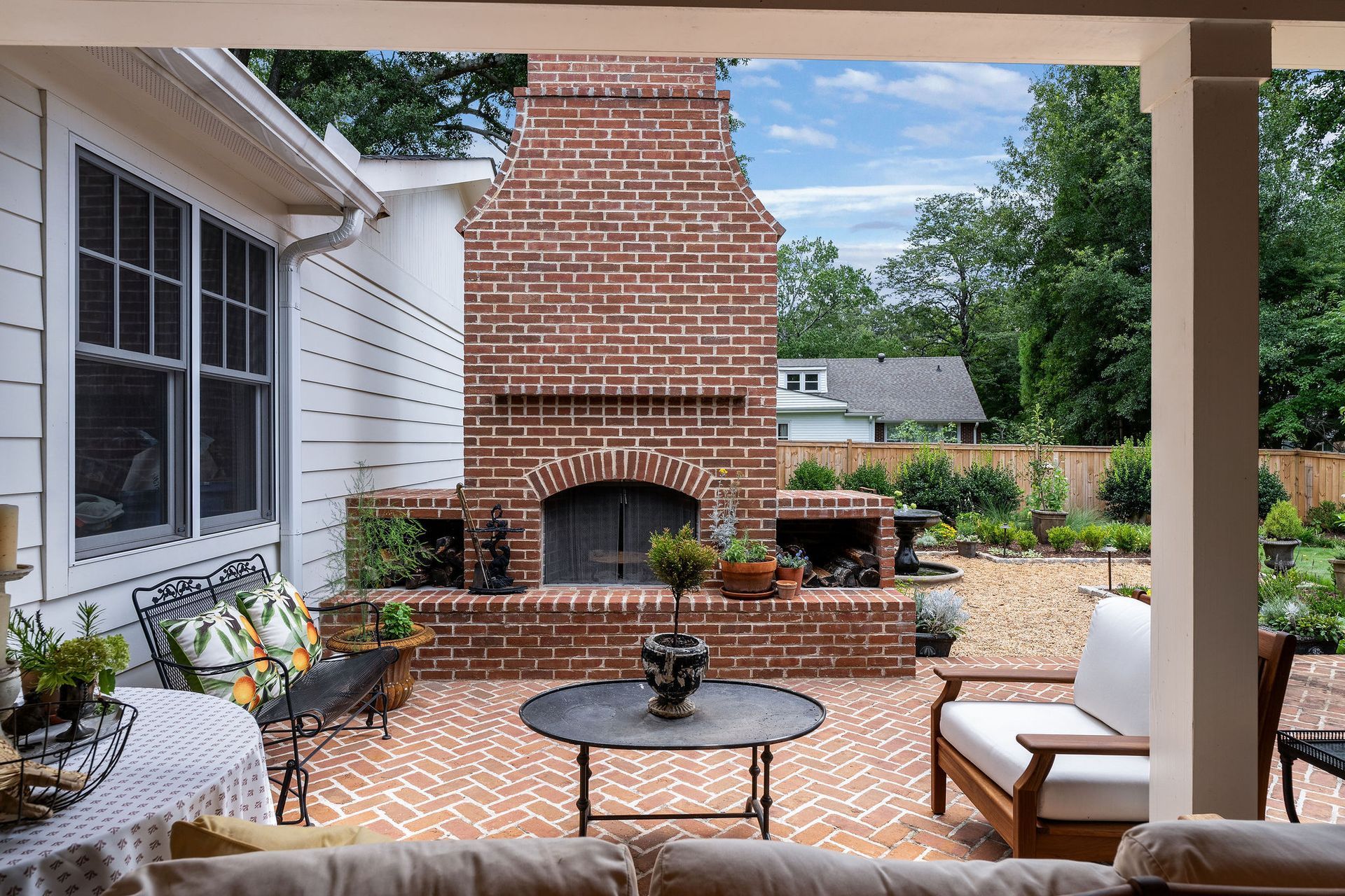 Covered patio with brick outdoor fireplace, herringbone brick floor, and wicker seating overlooking a garden