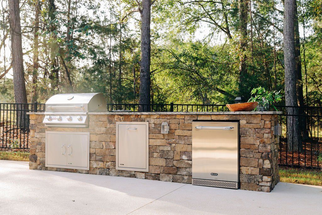 Outdoor stone outdoor kitchen with stainless grill and sink in a wooded backyard