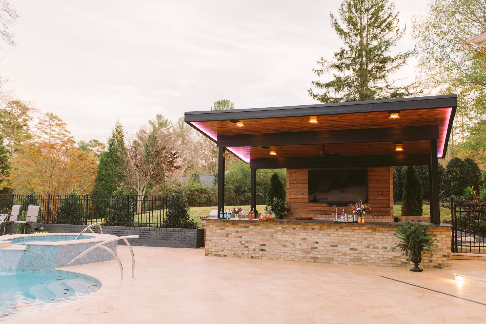 Modern backyard patio with pool, stone bar, and wood-roofed pavilion at sunset