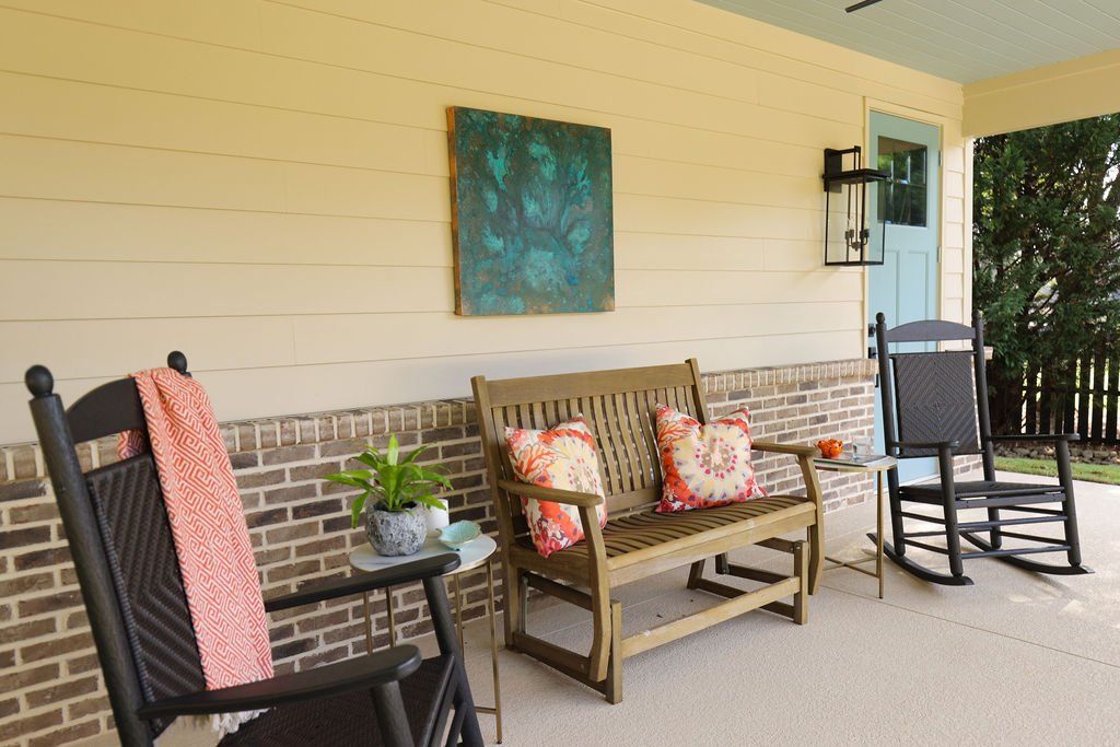 Covered porch with black rocking chairs, cushioned bench, and brick half-wall