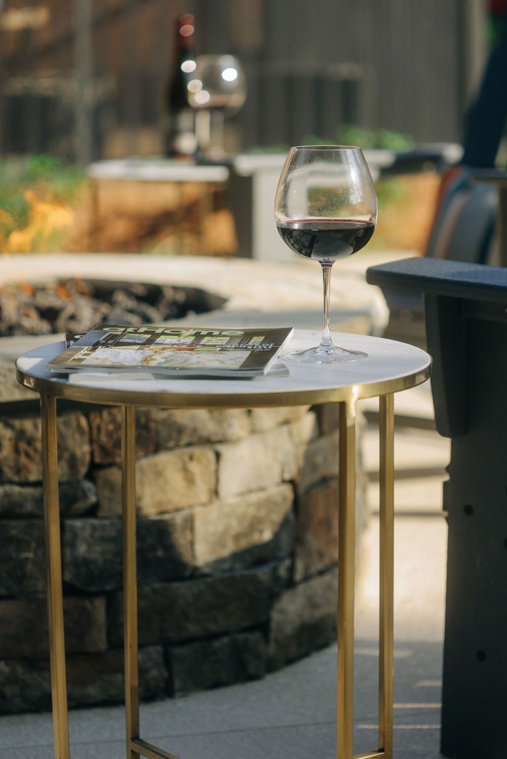 Wine glass on a small café table beside a magazine, with a stone planter in the background.