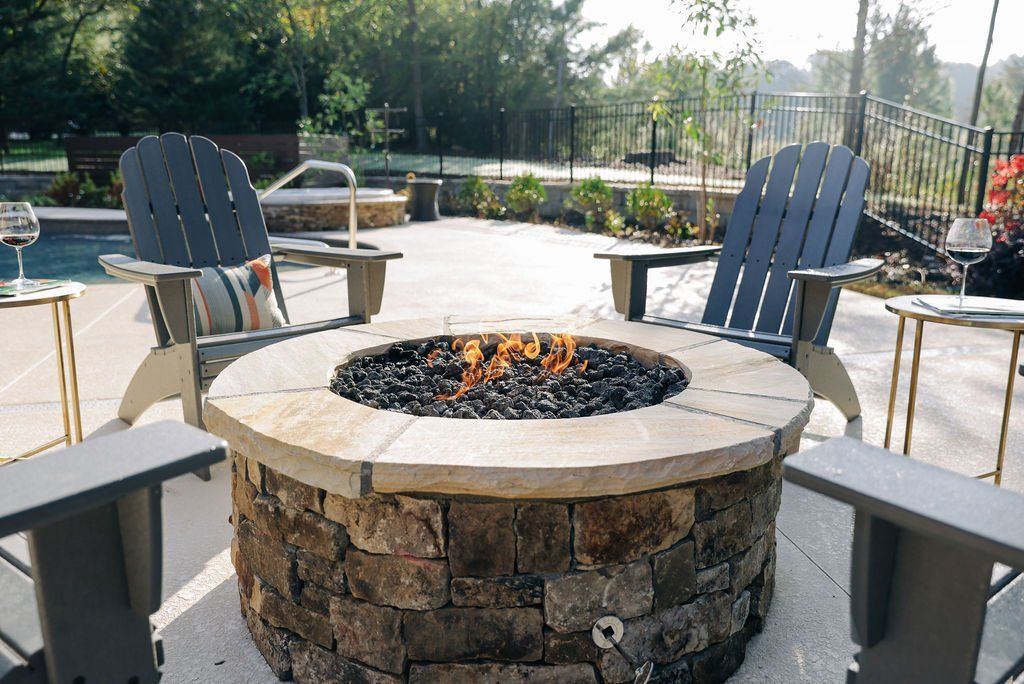 Patio fire pit with stone seating and Adirondack chairs in a sunny outdoor lounge area