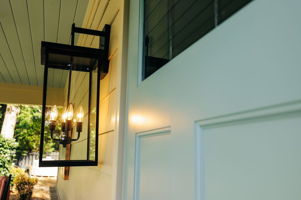Black lantern wall sconce beside a white paneled door on a porch at dusk
