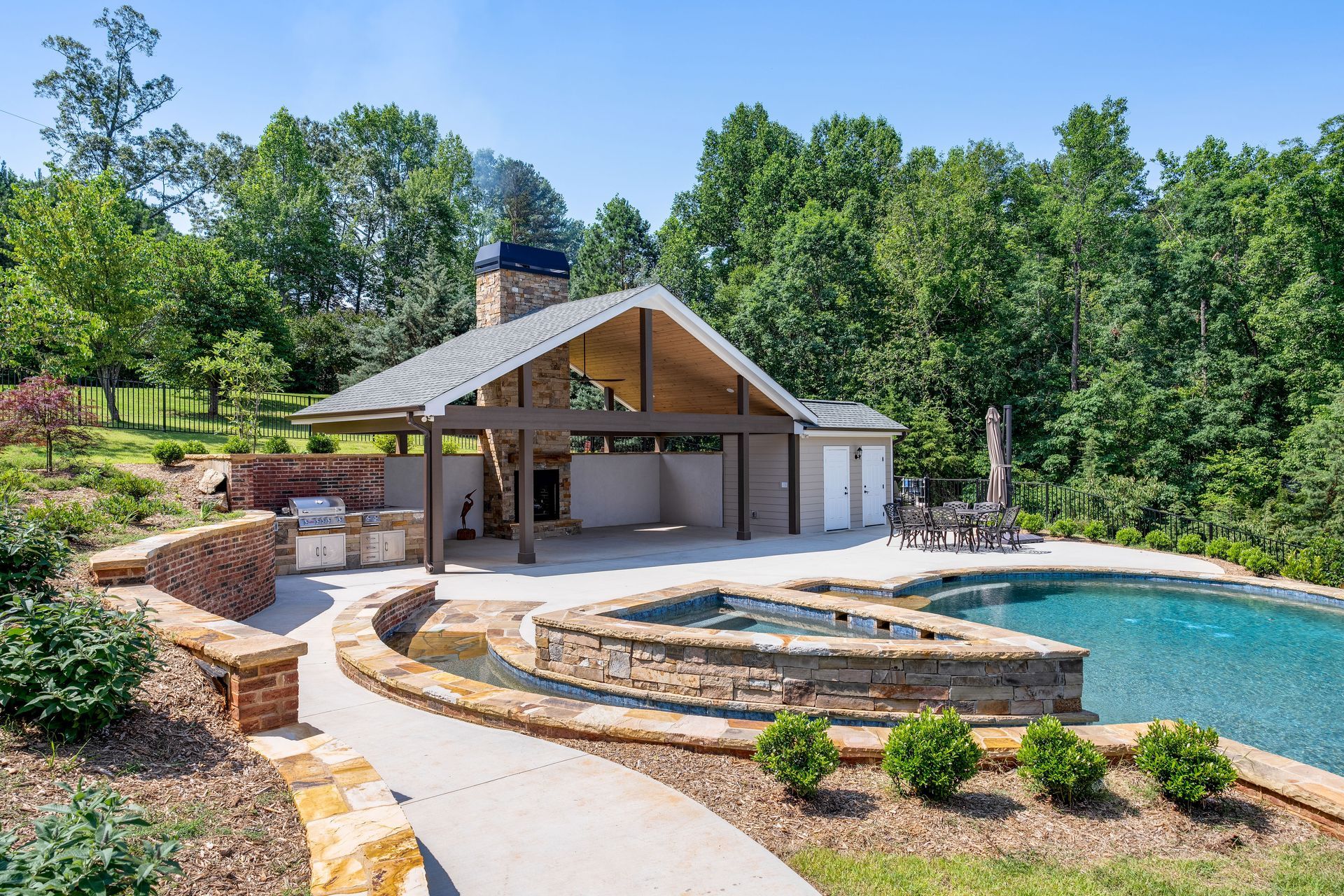 Modern backyard pool and stone patio with a covered pavilion and landscaped steps overlooking Lake Keowee