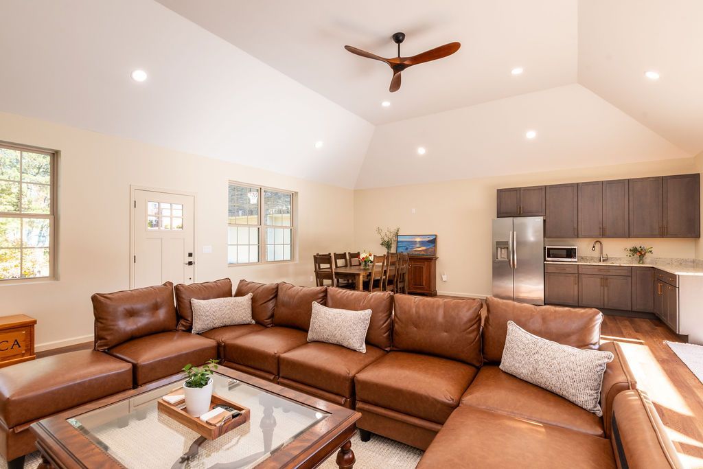 Spacious living room with brown sectional sofa, coffee table, dining area, and kitchen in poolhouse