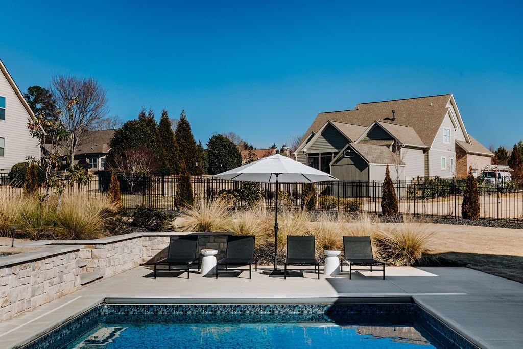 Backyard pool with lounge chairs and umbrella, overlooking houses under a clear blue sky