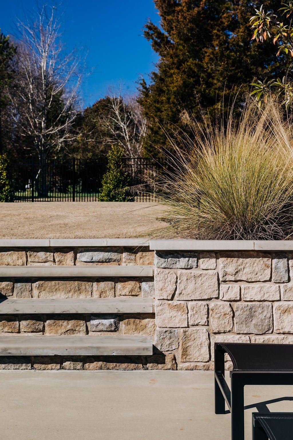 Stone patio with low retaining wall and ornamental grasses in a sunny park setting