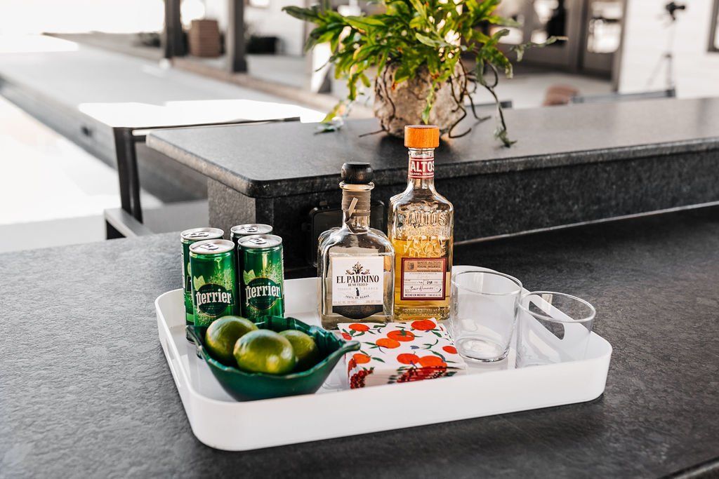 Tray with drinks, limes, and snacks on a black countertop in a modern kitchen-like setting