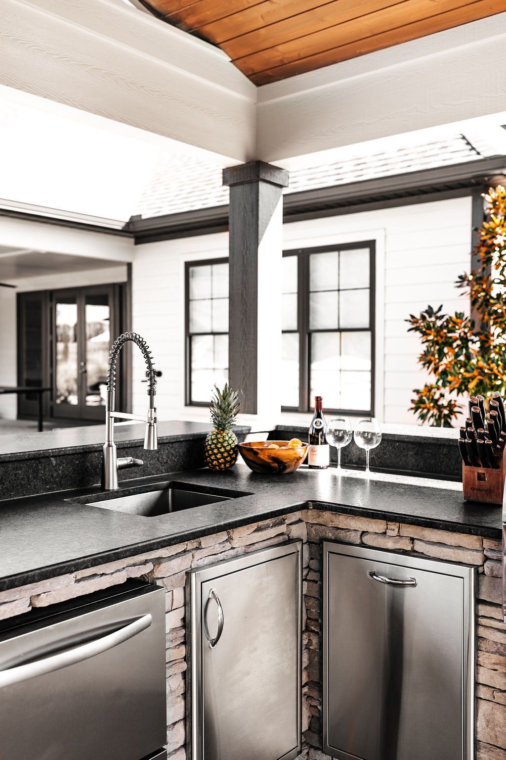 Modern kitchen corner with stainless appliances, black countertops, and white-framed windows.