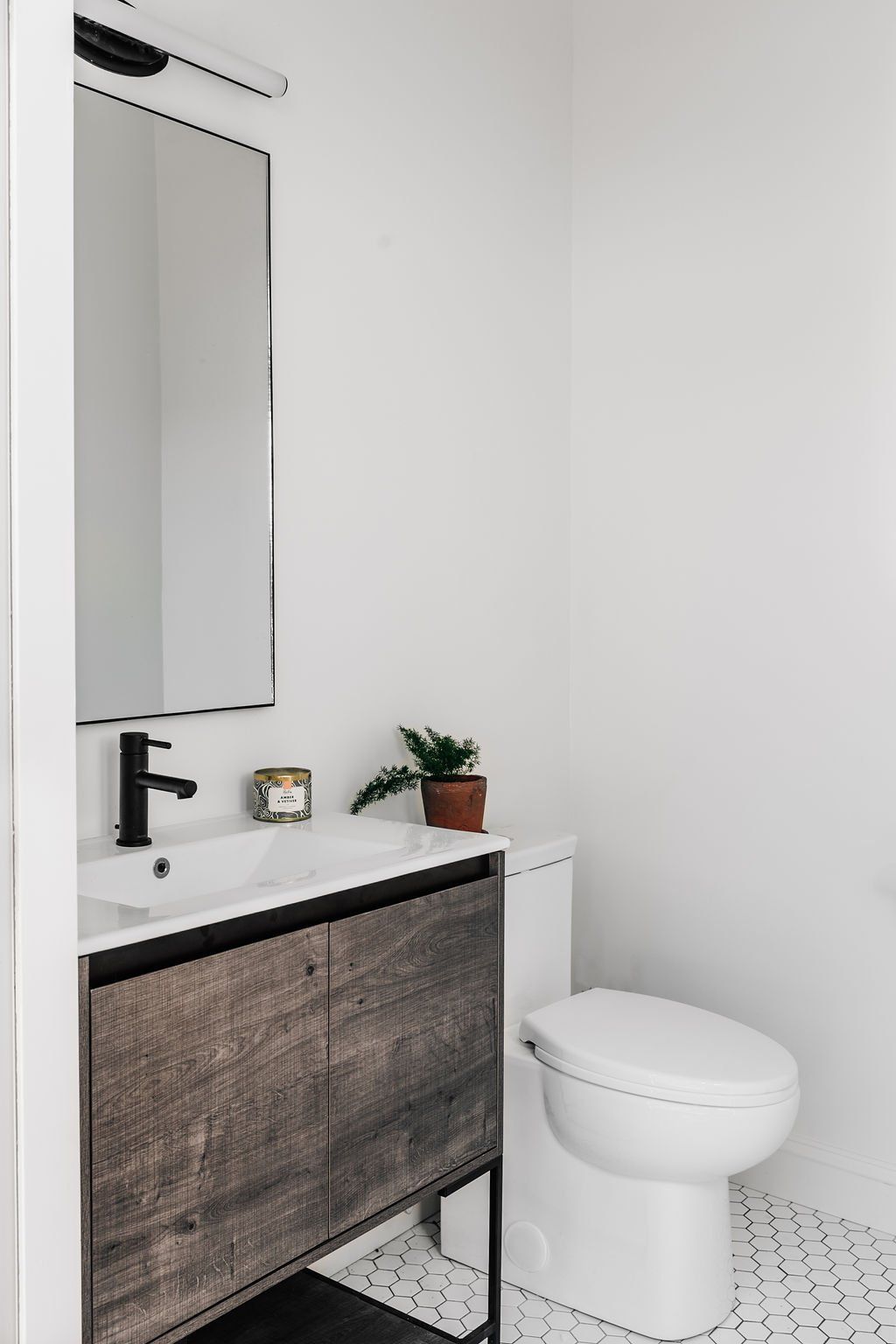 Modern bathroom with white toilet, vanity sink, mirror, and gray cabinet against white walls.