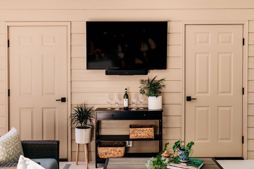 Living room wall with mounted TV, two beige doors, console table, and plants in front of a sofa