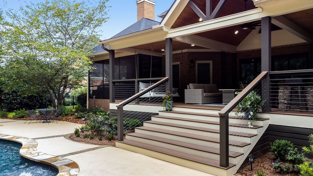 Front porch of a house with stone steps, railings, and landscaped yard beside a pool