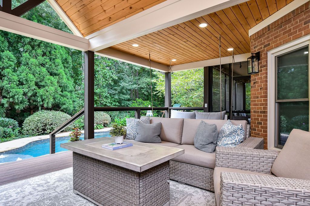 Covered outdoor patio with wicker seating, beige cushions, and a pool view under a wood-paneled ceiling.
