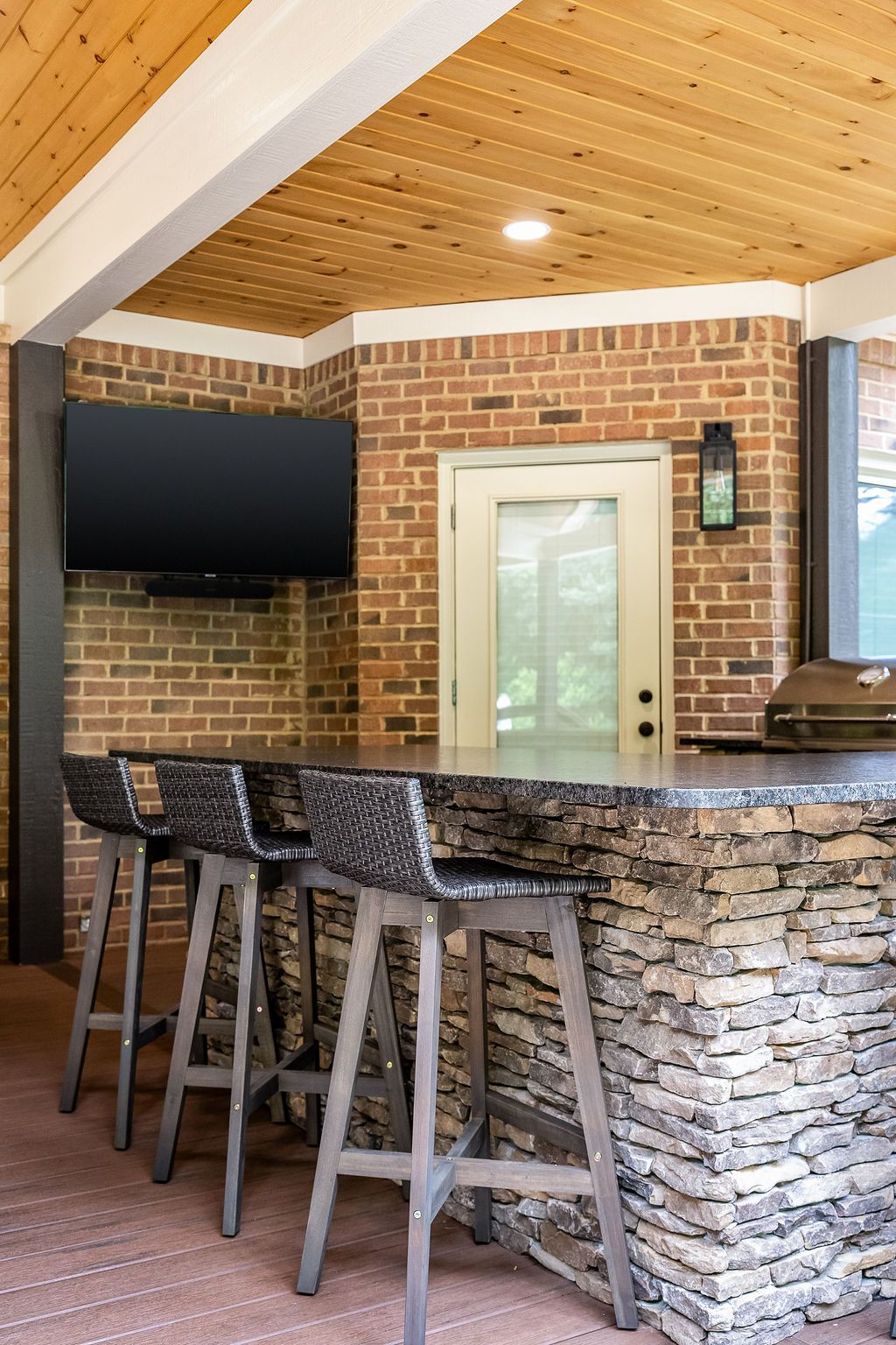 Modern bar area with stone-front counter, wooden stools, brick walls, and wall-mounted TV