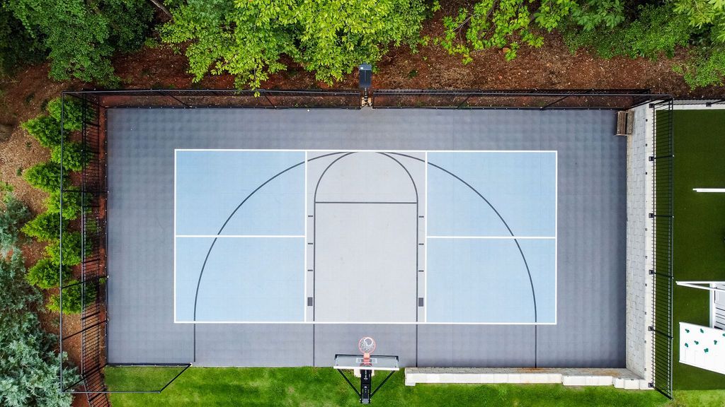 Aerial view of an empty outdoor basketball court bordered by trees and a soccer field.