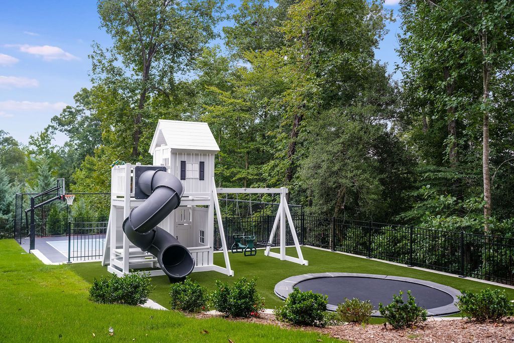 Children’s playground with white play structure, black slide, swings, and green trees in a park