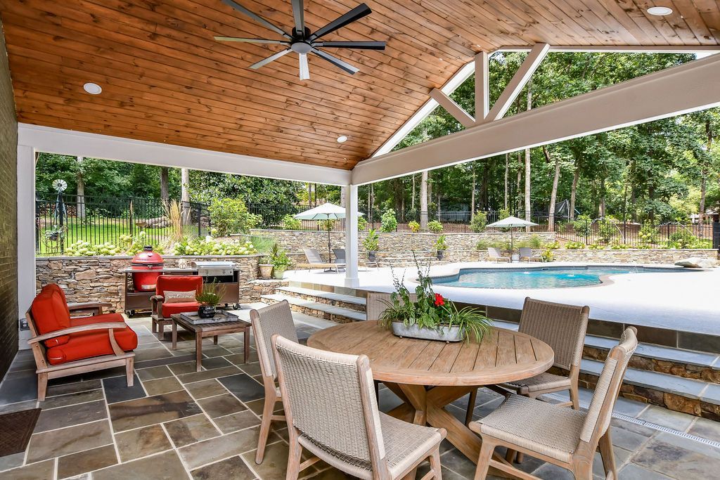 Covered patio with wicker seating and round table overlooking a pool and tropical trees